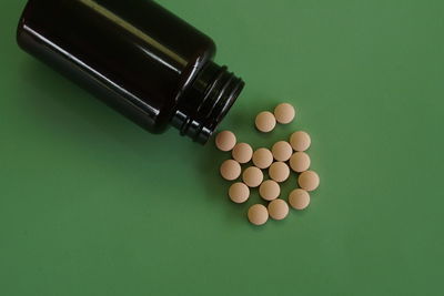 Close-up of pills spilling from bottle against green background