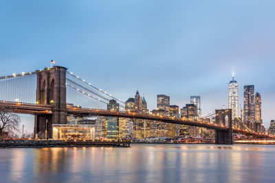 Illuminated bridge over river against sky in city