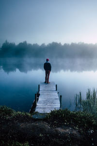 Rear view of man standing on pier over lake against sky