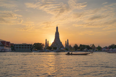 Scenic view of river by buildings against sky during sunset