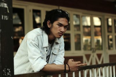 Portrait of young man looking away while sitting on railing