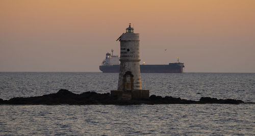 Lighthouse by sea against sky during sunset