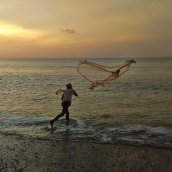 Man jumping on beach against sky during sunset