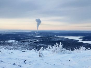Smoke emitting from chimney on snowcapped landscape against sky