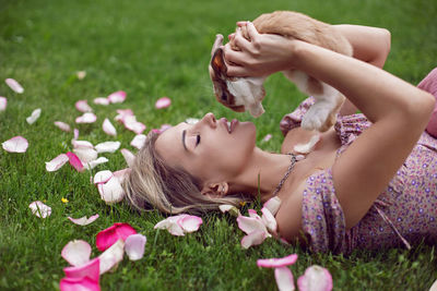 Portrait of a beautiful young woman lying on a green meadow and holding a rabbit in her hands
