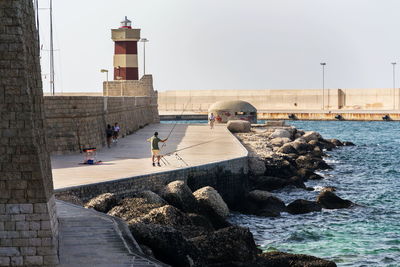 People on rock by sea against clear sky