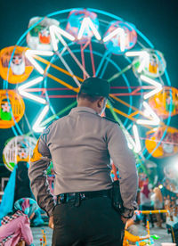 Rear view of man standing against illuminated ferris wheel at night
