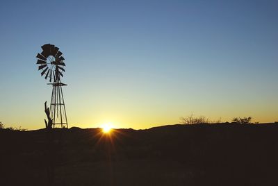 American-style windmill on field against clear sky during sunset