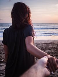 Rear view of woman standing at beach during sunset