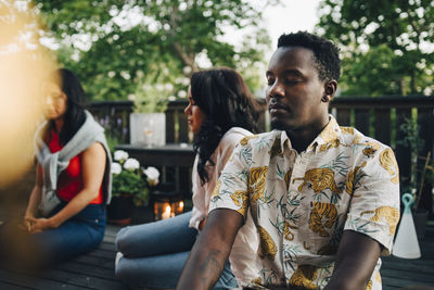 Multi-ethnic friends sitting with eyes closed in balcony during group session at weekend
