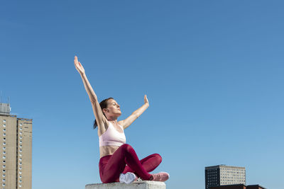 Sporty woman sitting with her arms raised and eyes closed enjoying the freedom.