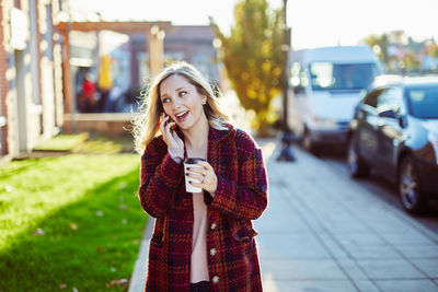 Young woman holding drink while standing in city