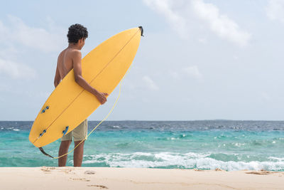 Male surfer standing on shore against sea at beach