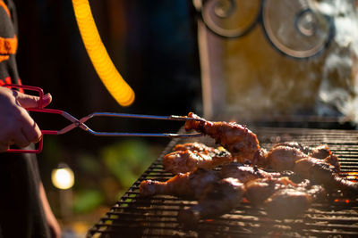 Person holding meat on barbecue grill