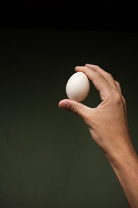 Close-up of hand holding egg against black background