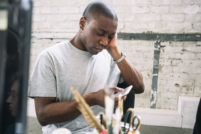 Young male hacker using smart phone while sitting at creative workplace