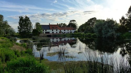 Scenic view of lake by trees and buildings against sky