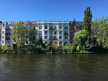 Buildings by river against clear blue sky