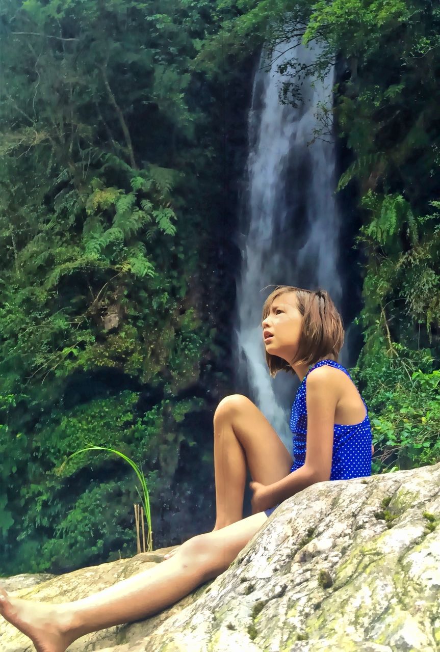 young adult, lifestyles, leisure activity, young women, sitting, rock - object, person, casual clothing, tree, relaxation, waterfall, water, three quarter length, full length, looking at camera, portrait, waist up, nature