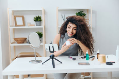 Happy woman filming make-up tutorial through camera at home