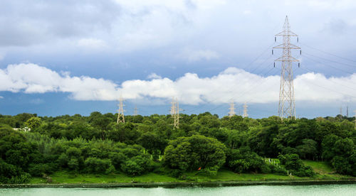 Electricity pylon by trees against sky