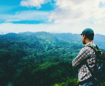 Side view of young man looking at mountains against sky