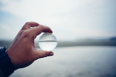 Close-up of hand holding crystal ball at beach against sky