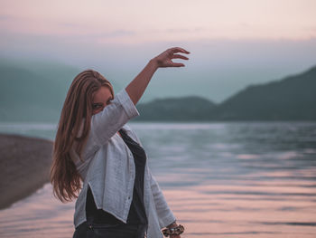 Woman standing by lake against sky during sunset