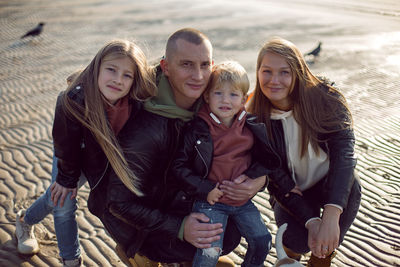 Family in a leather jacket stands along the beach with their dog in autumn