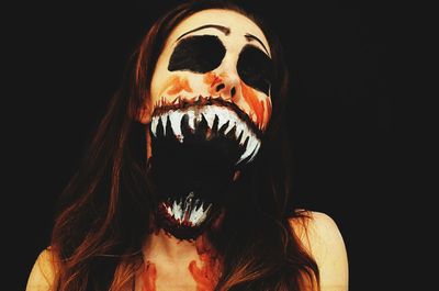 Close-up of woman with spooky face paint against black background