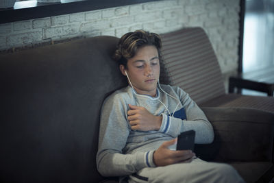Full length of young man using mobile phone while sitting on sofa