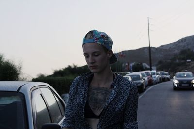 Close-up of young woman standing by car against sky