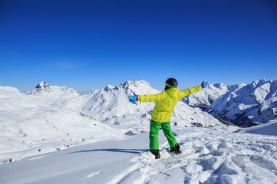 Rear view of young man with arms outstretched standing on snowcapped mountain