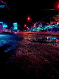 Illuminated road by buildings against sky at night