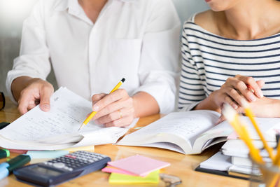 Midsection of friends studying on desk