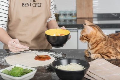 The woman owner and her cat lay out the pizza toppings on the dough.