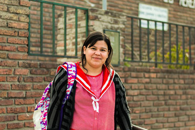 Portrait of smiling woman standing against brick wall