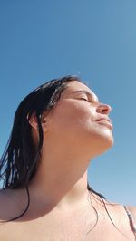 Low angle view of young woman against clear blue sky
