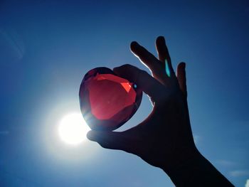 Cropped image of hand holding gen against sky on sunny day