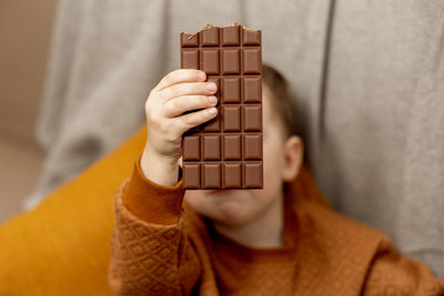 Little adorable boy sitting on the couch at home and eating chocolate bar. child and sweets