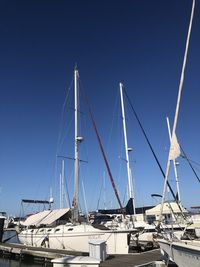Sailboats moored at harbor against clear blue sky