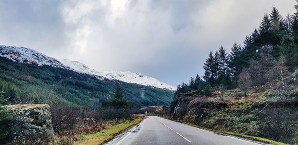 Empty road by snowcapped mountains against sky