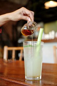 Midsection of person pouring drink in glass on table