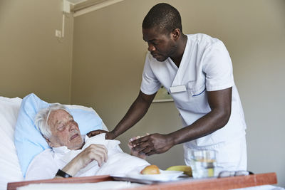 Male nurse giving cough syrup to senior man in hospital ward