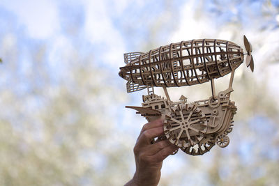 Close-up of hand holding metal against sky