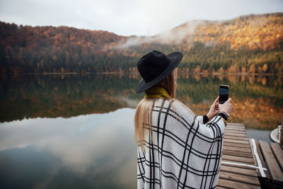 Rear view of person photographing against sky in lake