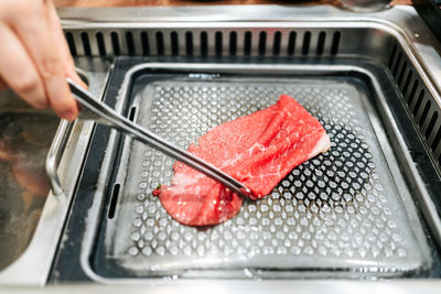 Hand grilling a medium rare slice of kagoshima wagyu a5 beef with marble texture with tongs.