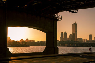 Bridge over river with buildings in background at sunset