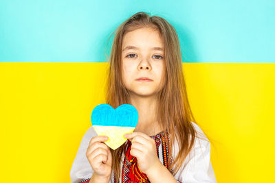 
a girl in a national ukrainian vyshyvanka holds a heart painted in yellow and blue tones.