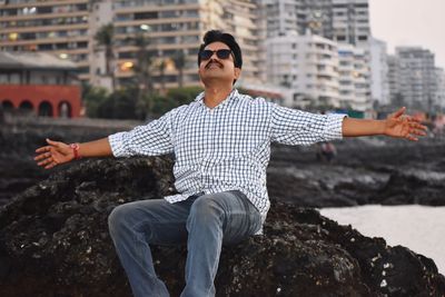 Young man with sunglasses on rock in city